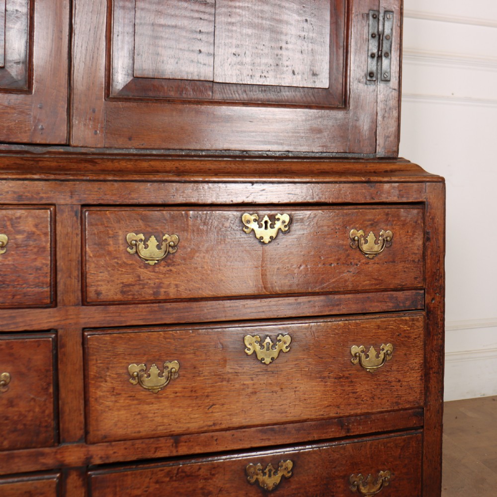 An antique two-part English oak linen press featuring upper fielded panel cupboard doors and a base with six drawers fitted with brass drop handles. View VI