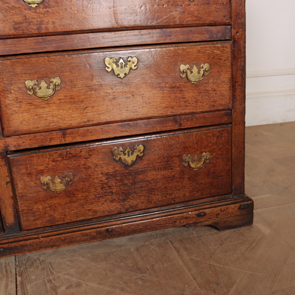 An antique two-part English oak linen press featuring upper fielded panel cupboard doors and a base with six drawers fitted with brass drop handles. View VII