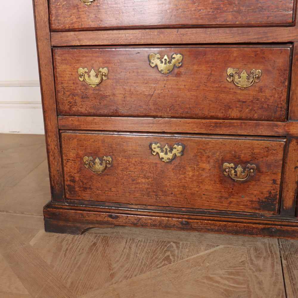 An antique two-part English oak linen press featuring upper fielded panel cupboard doors and a base with six drawers fitted with brass drop handles. View VIII