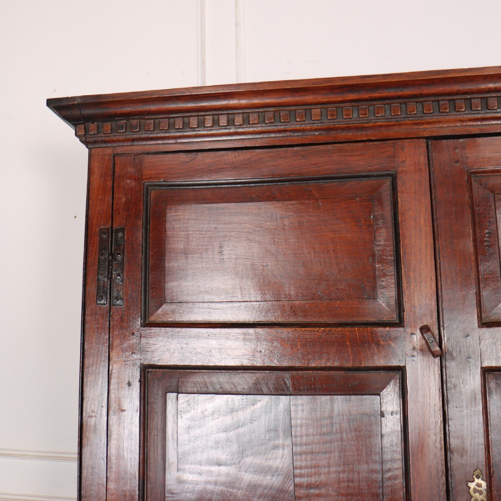 An antique two-part English oak linen press featuring upper fielded panel cupboard doors and a base with six drawers fitted with brass drop handles. View IX