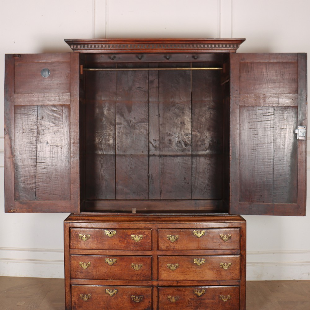 An antique two-part English oak linen press featuring upper fielded panel cupboard doors and a base with six drawers fitted with brass drop handles. View XI