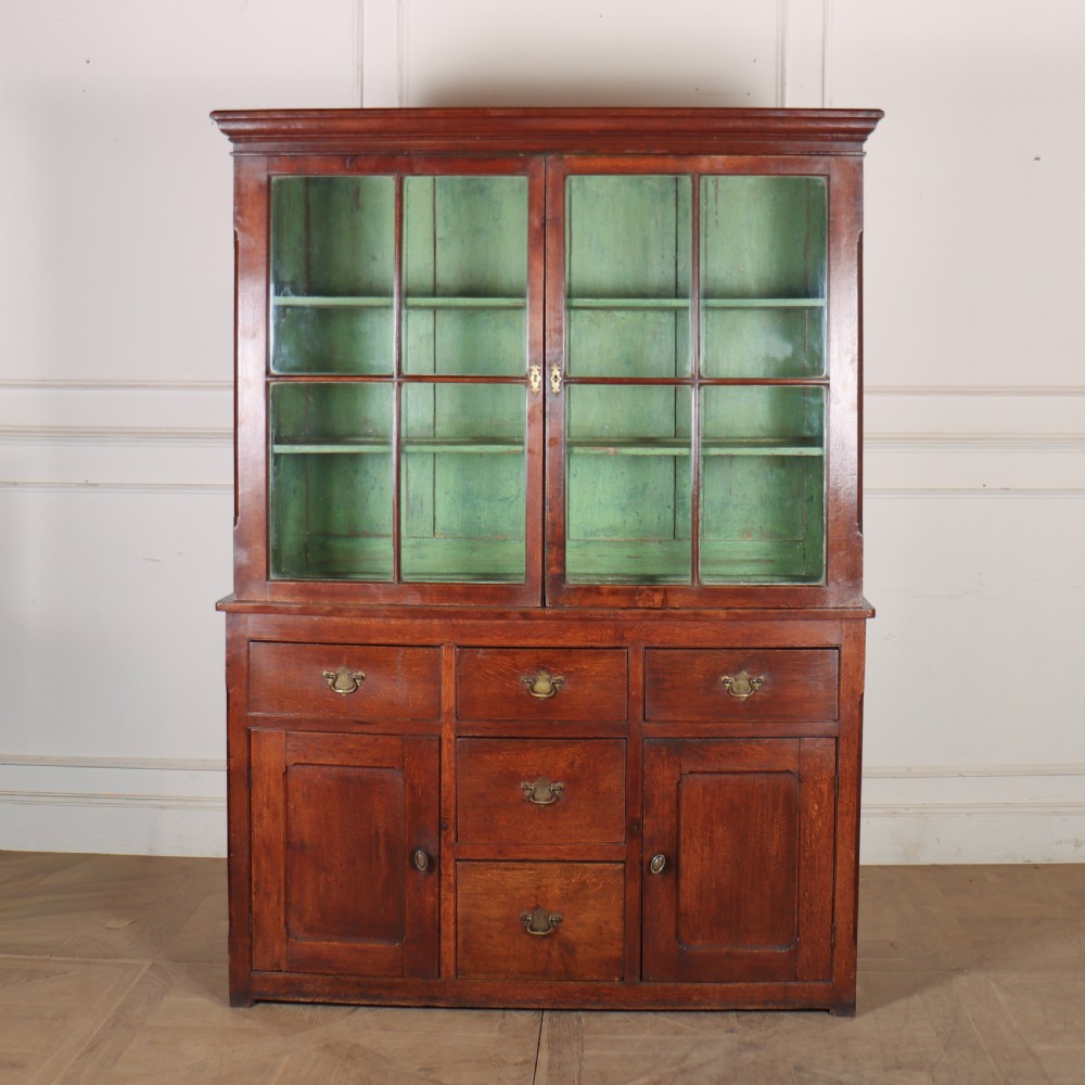 A large two-part oak kitchen dresser with a glazed upper section featuring a green painted interior above a base with five drawers and two panelled cupboard doors.