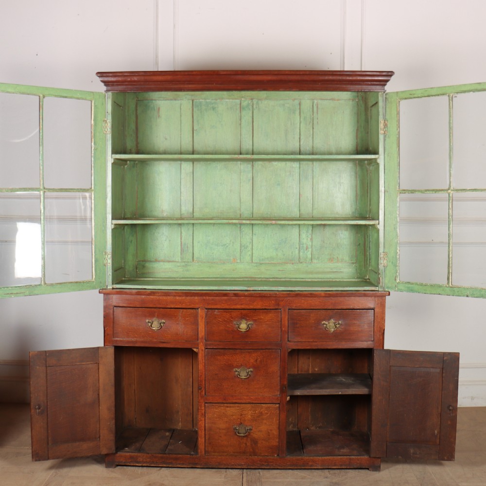 A large two-part oak kitchen dresser with a glazed upper section featuring a green painted interior above a base with five drawers and two panelled cupboard doors. View VI