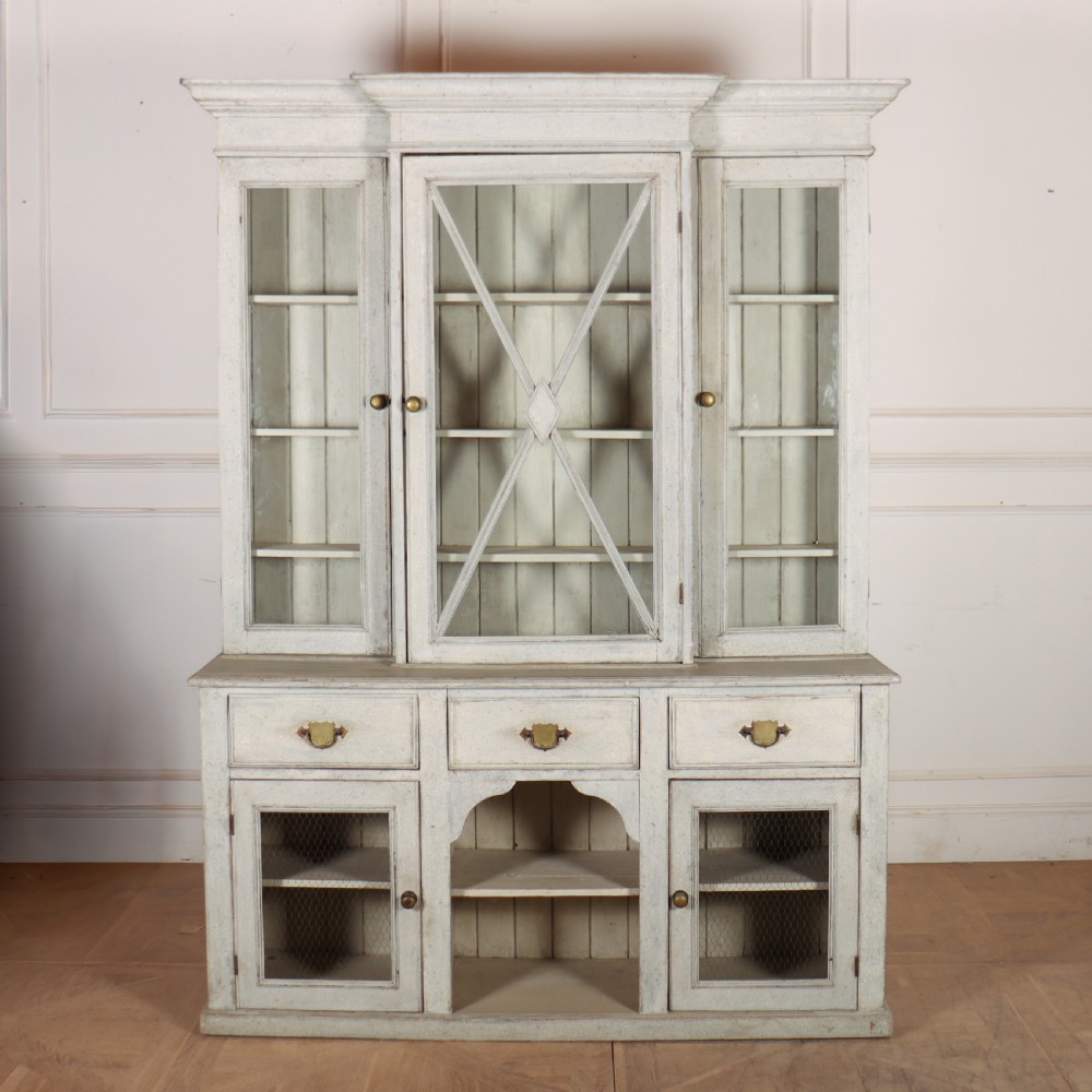A painted off-white breakfront kitchen dresser featuring glazed upper doors, a central X-mullion door, three drawers, and lower wire mesh cupboards.