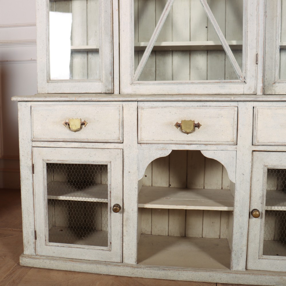A painted off-white breakfront kitchen dresser featuring glazed upper doors, a central X-mullion door, three drawers, and lower wire mesh cupboards. View II