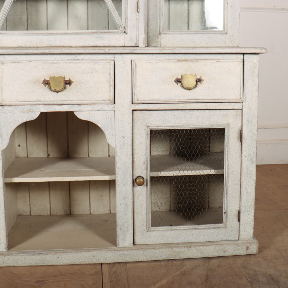 A painted off-white breakfront kitchen dresser featuring glazed upper doors, a central X-mullion door, three drawers, and lower wire mesh cupboards. View V