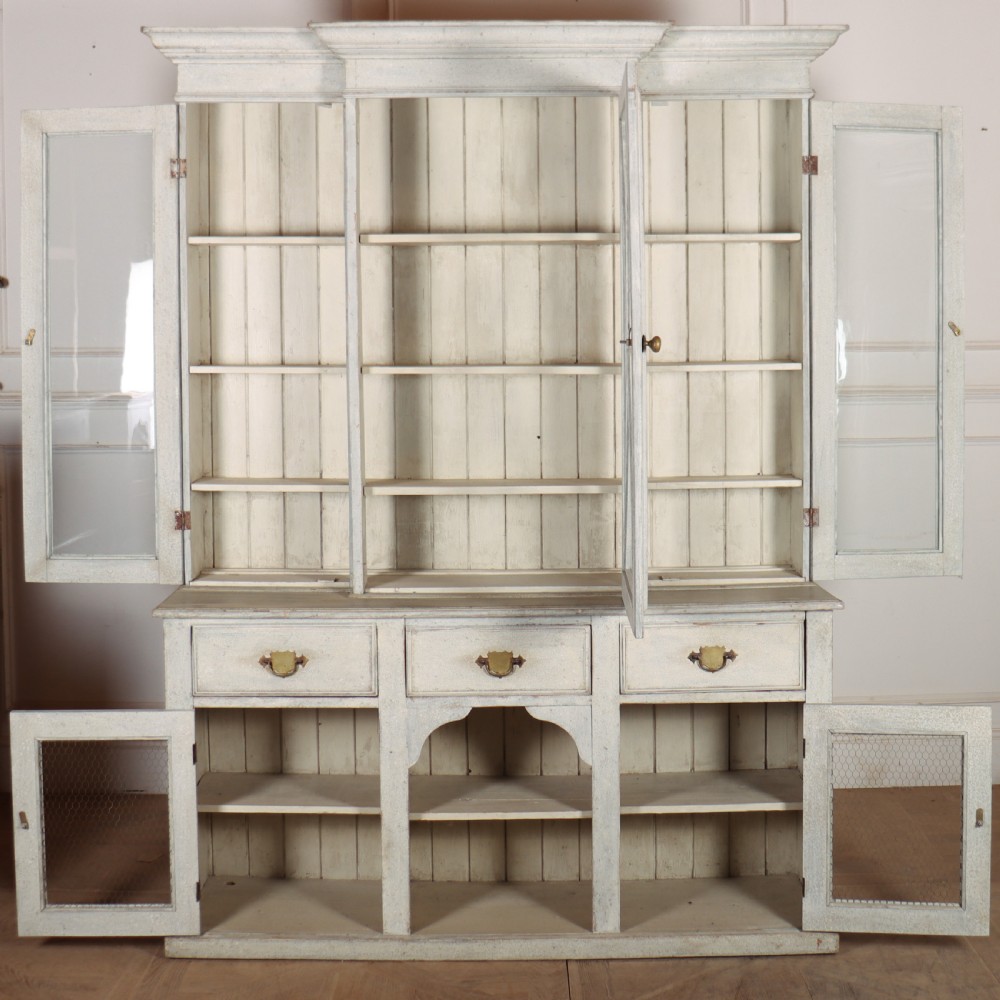 A painted off-white breakfront kitchen dresser featuring glazed upper doors, a central X-mullion door, three drawers, and lower wire mesh cupboards. View VIII