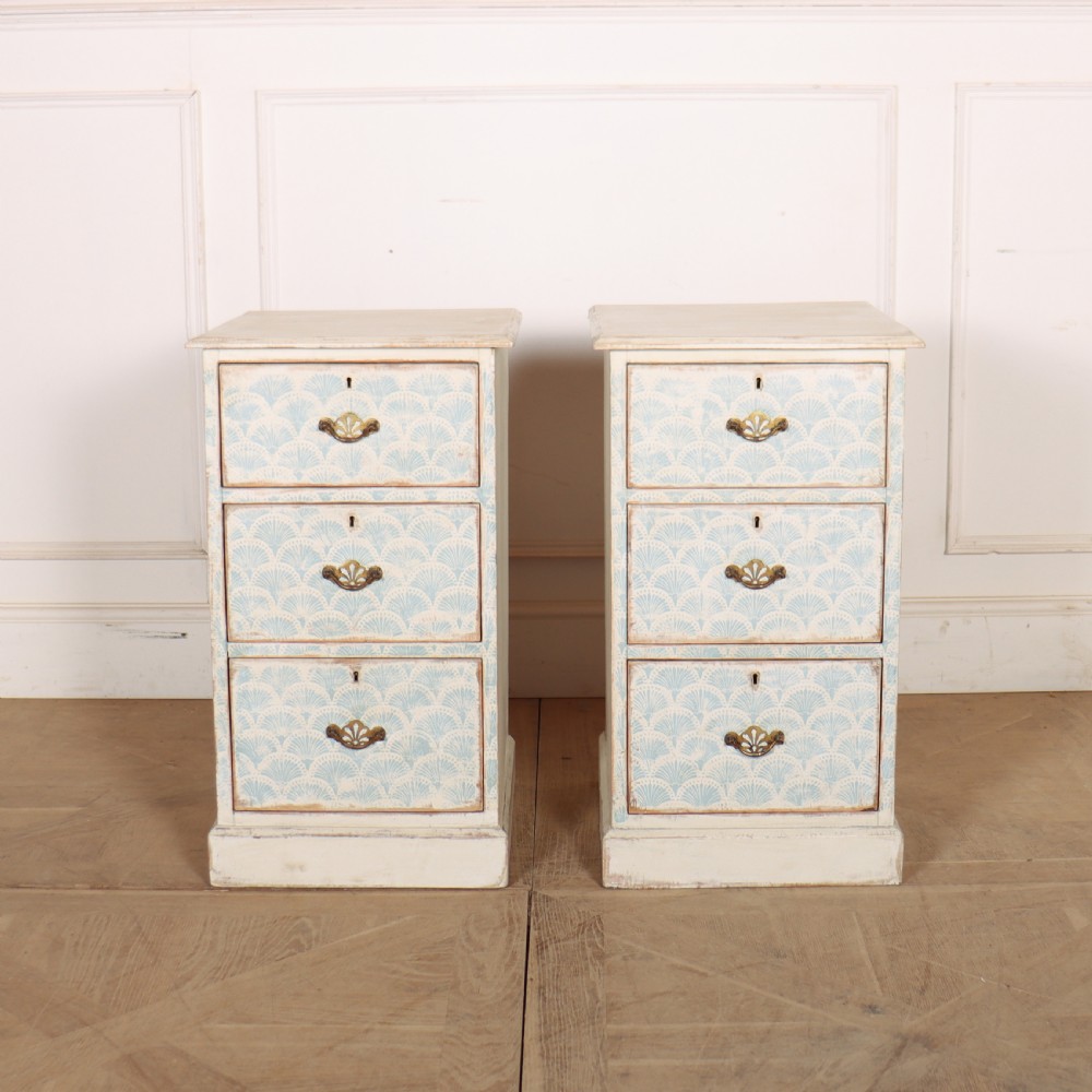 A pair of narrow three-drawer wooden chests featuring off-white distressed paint finish, brass handles, and blue hand-painted fan pattern drawer fronts.