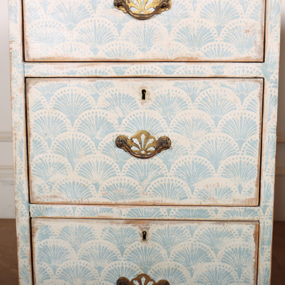 A pair of narrow three-drawer wooden chests featuring off-white distressed paint finish, brass handles, and blue hand-painted fan pattern drawer fronts. View VI