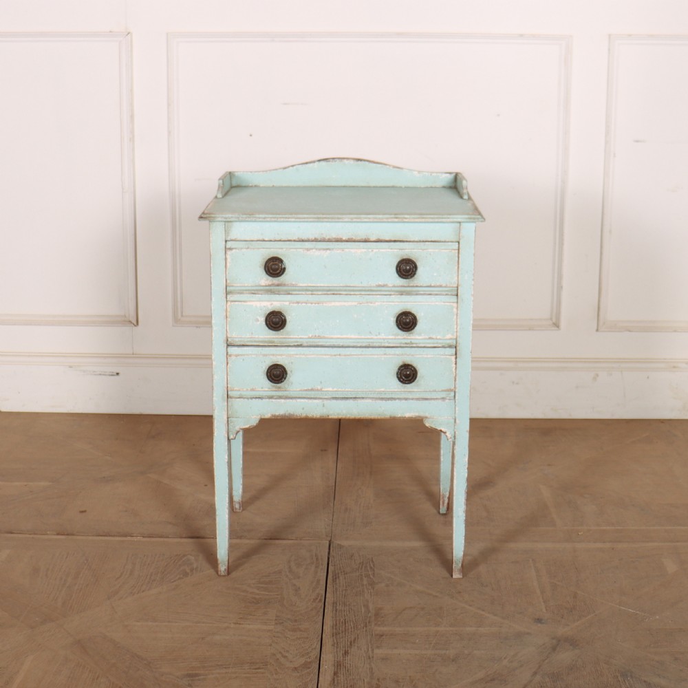 A pale blue painted three-drawer antique bedside cabinet featuring dark round knobs and a low gallery top.