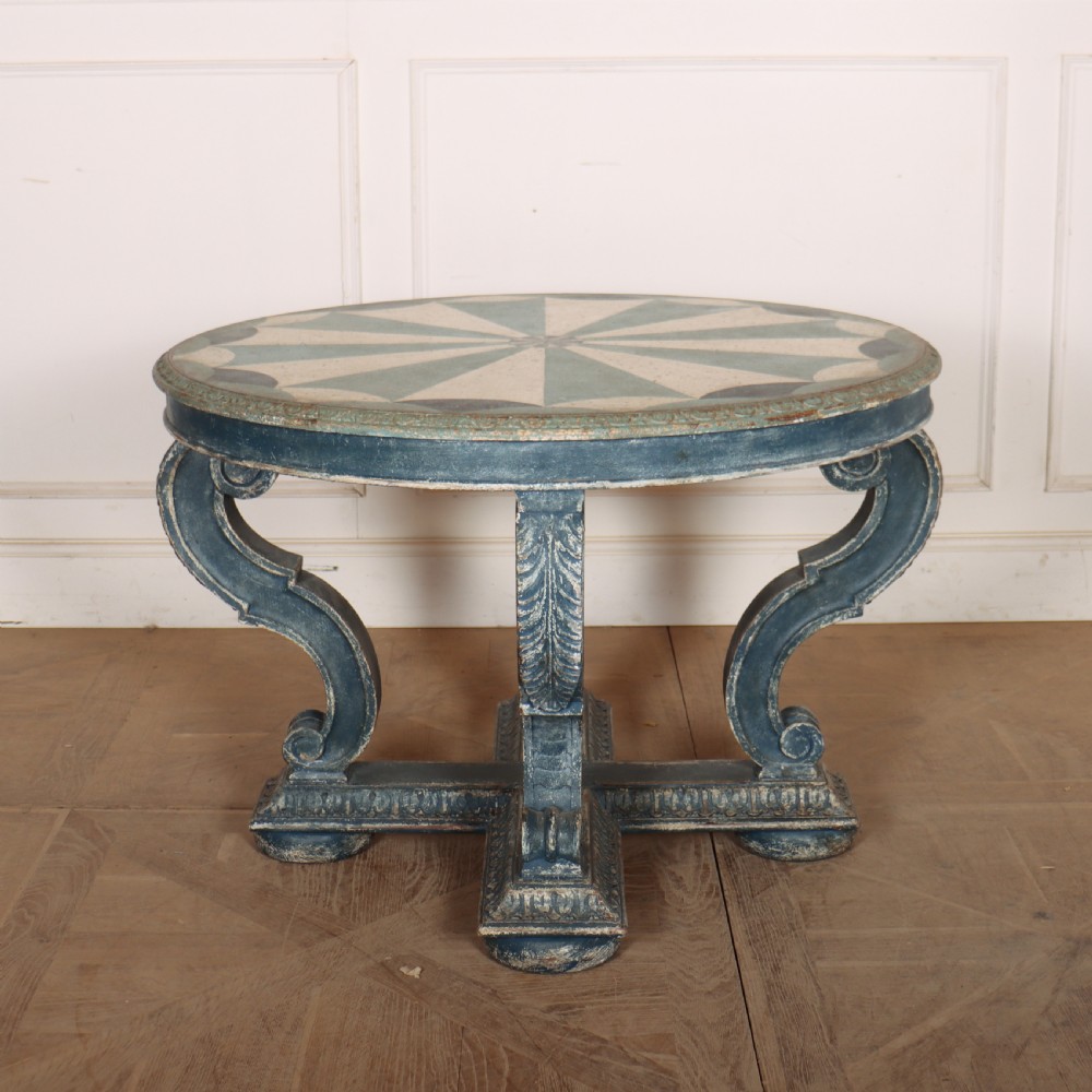 A round blue painted lamp table featuring a starburst pattern top, carved scroll legs, and an X-frame base.