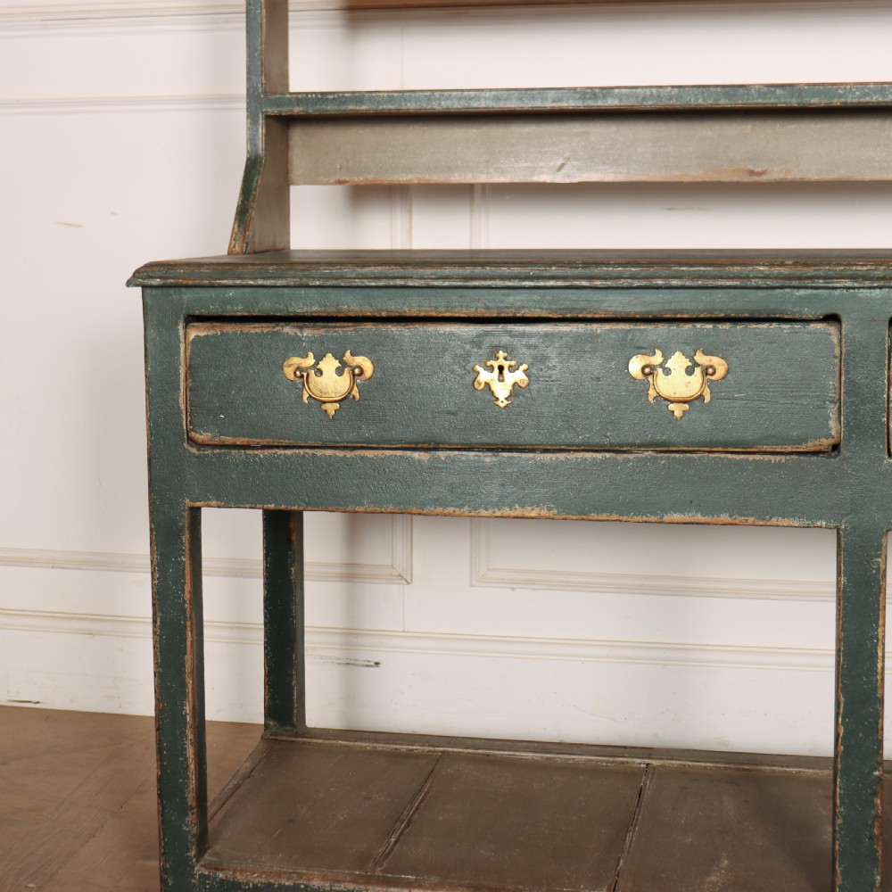 An antique dark green painted wooden pot board dresser featuring an upper three-tier plate rack with cup hooks above two drawers and an open bottom shelf. View II