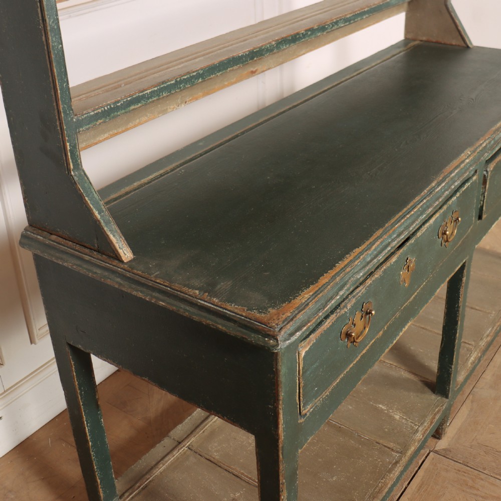 An antique dark green painted wooden pot board dresser featuring an upper three-tier plate rack with cup hooks above two drawers and an open bottom shelf. View X