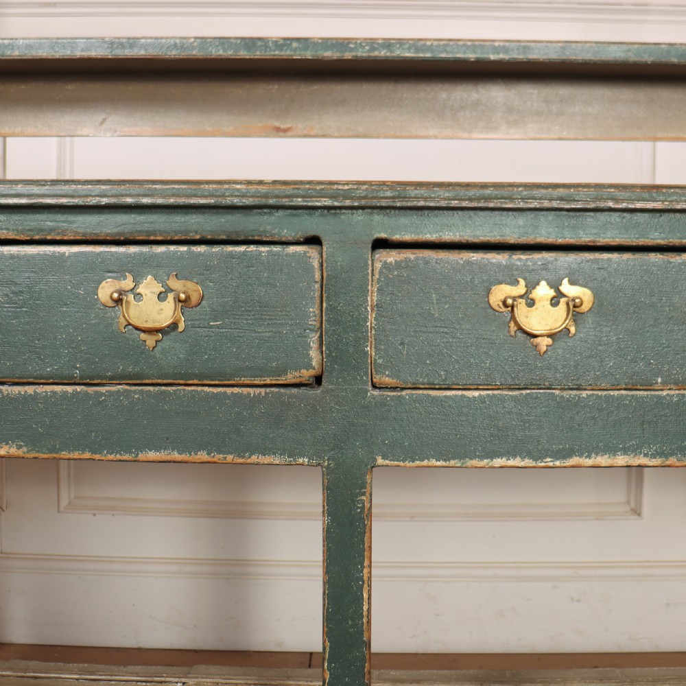 An antique dark green painted wooden pot board dresser featuring an upper three-tier plate rack with cup hooks above two drawers and an open bottom shelf. View XIV