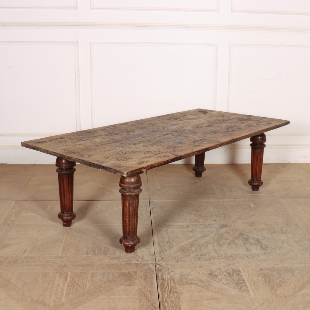 A low rectangular wooden coffee table featuring turned reeded legs and a surface decorated with carved typography and circular details.