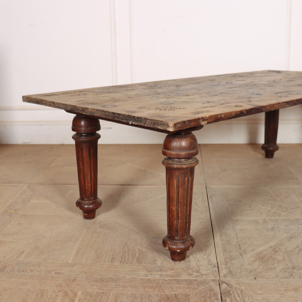 A low rectangular wooden coffee table featuring turned reeded legs and a surface decorated with carved typography and circular details. View II