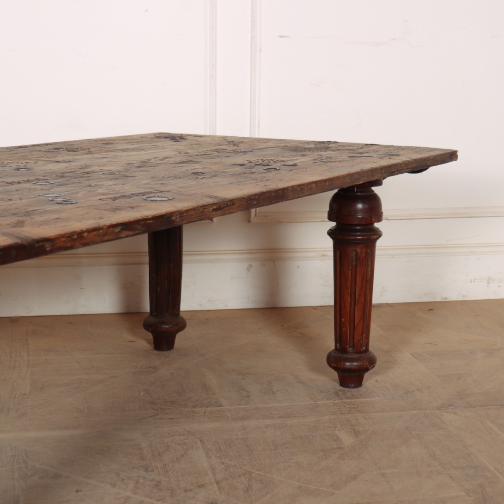 A low rectangular wooden coffee table featuring turned reeded legs and a surface decorated with carved typography and circular details. View III