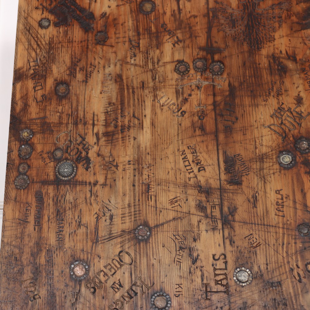 A low rectangular wooden coffee table featuring turned reeded legs and a surface decorated with carved typography and circular details. View VI
