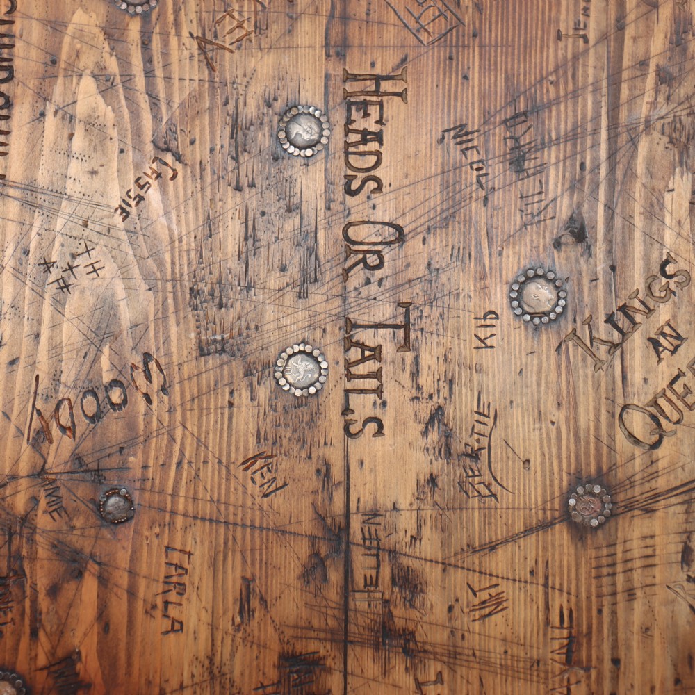 A low rectangular wooden coffee table featuring turned reeded legs and a surface decorated with carved typography and circular details. View XI