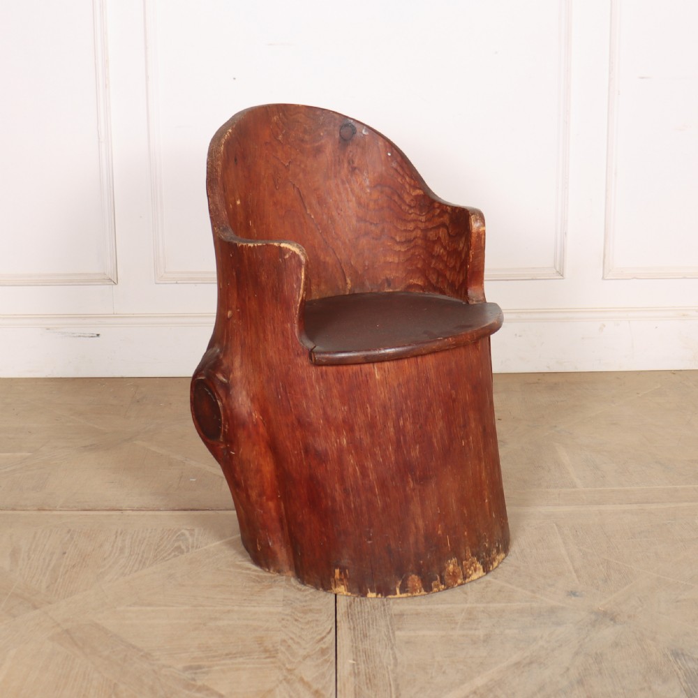 A Swedish dugout armchair carved from a single hollowed-out wooden tree trunk showing natural grain, knots, and a rounded seat.