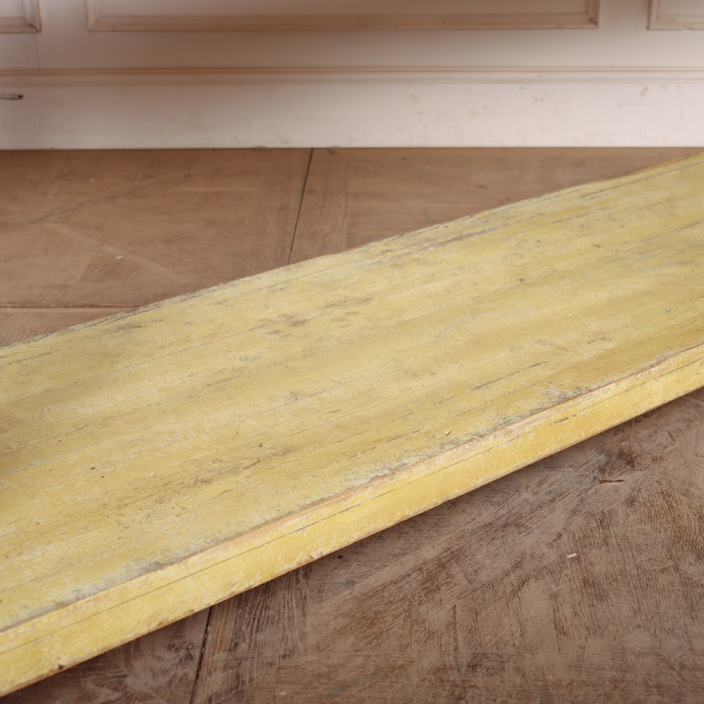 A long French drapers table featuring a natural wood plank top, a yellow painted apron and turned legs, and a low potboard shelf. View IV