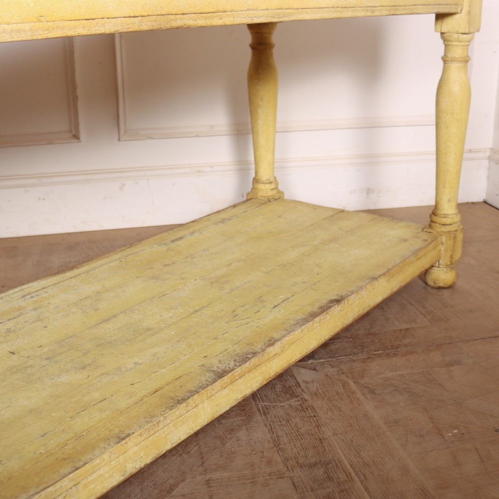 A long French drapers table featuring a natural wood plank top, a yellow painted apron and turned legs, and a low potboard shelf. View VI