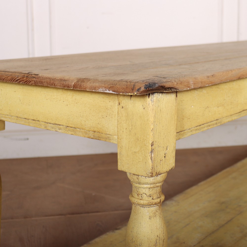 A long French drapers table featuring a natural wood plank top, a yellow painted apron and turned legs, and a low potboard shelf. View X