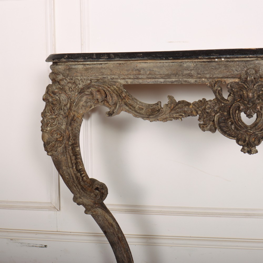 An Italian Rococo styled console table featuring heavily carved cabriole legs, a central apron cartouche motif, distressed grey paint finish, and a dark top. View II