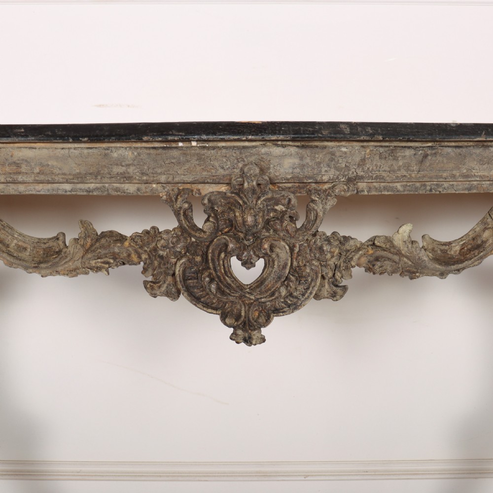 An Italian Rococo styled console table featuring heavily carved cabriole legs, a central apron cartouche motif, distressed grey paint finish, and a dark top. View IV