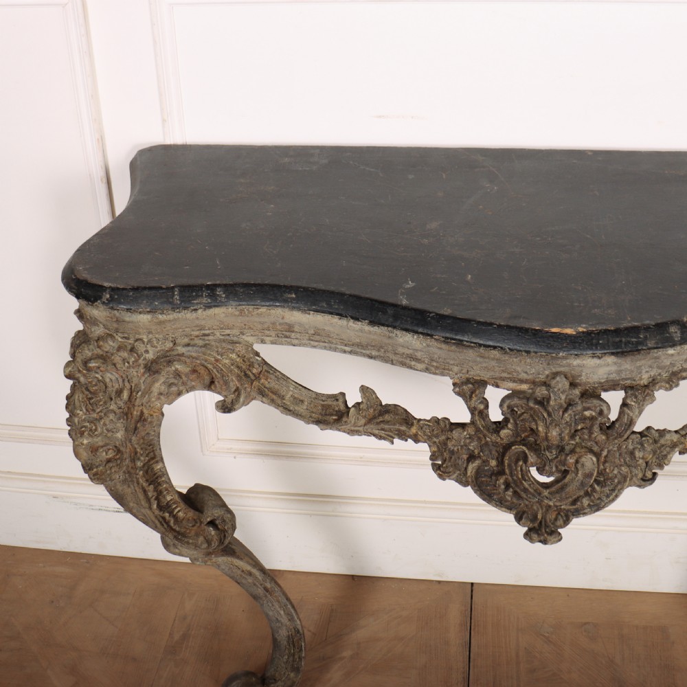 An Italian Rococo styled console table featuring heavily carved cabriole legs, a central apron cartouche motif, distressed grey paint finish, and a dark top. View VIII
