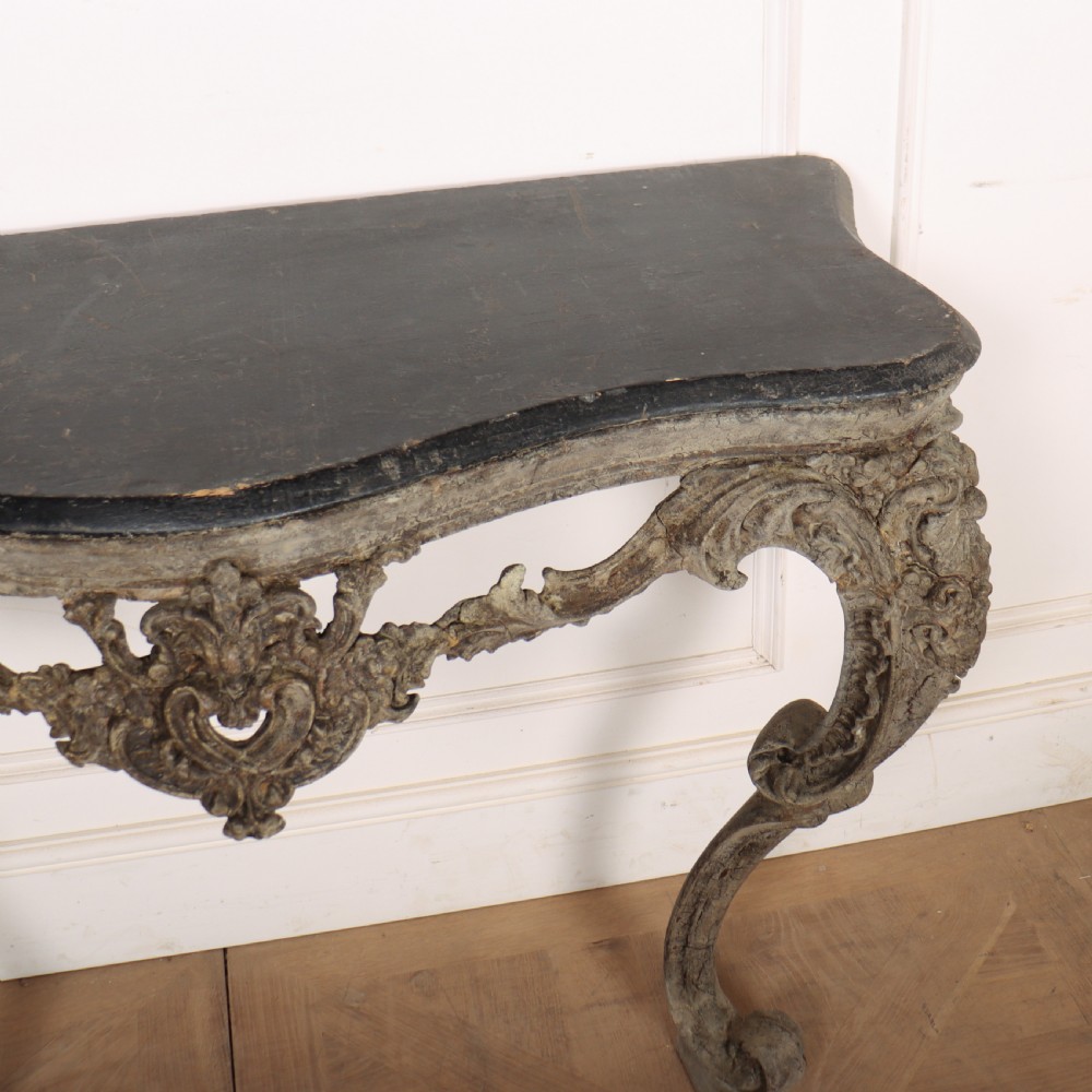 An Italian Rococo styled console table featuring heavily carved cabriole legs, a central apron cartouche motif, distressed grey paint finish, and a dark top. View IX