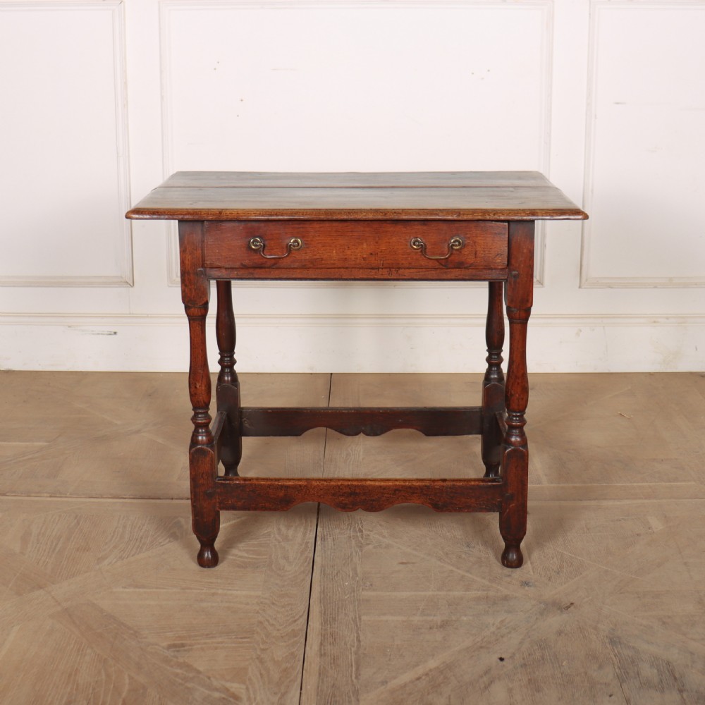 An antique English oak lamp table featuring a single drawer with brass handles, turned legs, and lower stretchers.