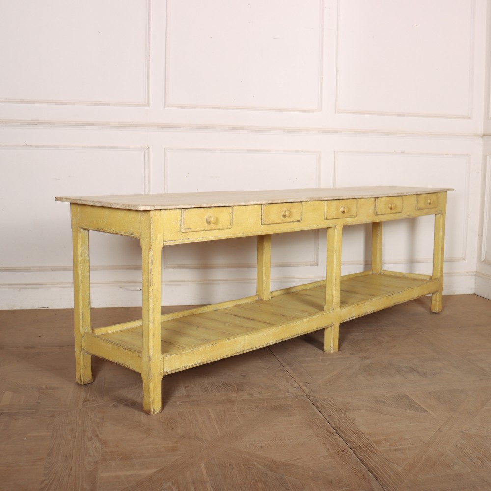 A long antique English painted wooden serving table featuring five drawers, a natural timber top, a distressed yellow base, and a low potboard shelf.