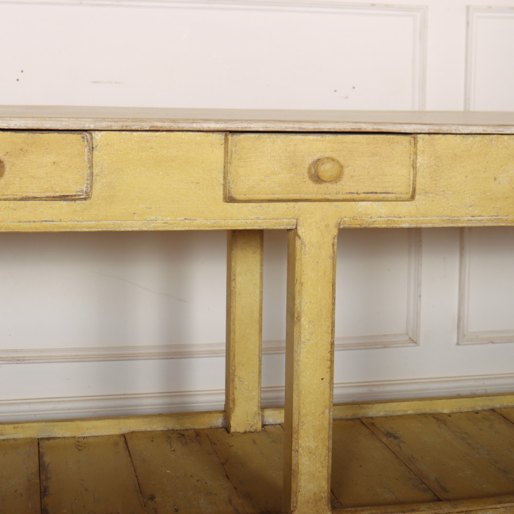 A long antique English painted wooden serving table featuring five drawers, a natural timber top, a distressed yellow base, and a low potboard shelf. View VII