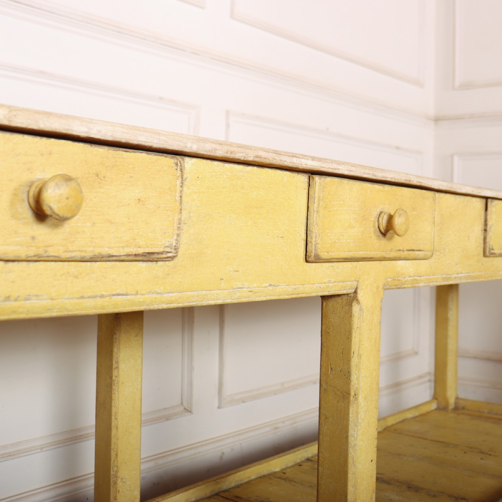 A long antique English painted wooden serving table featuring five drawers, a natural timber top, a distressed yellow base, and a low potboard shelf. View XII