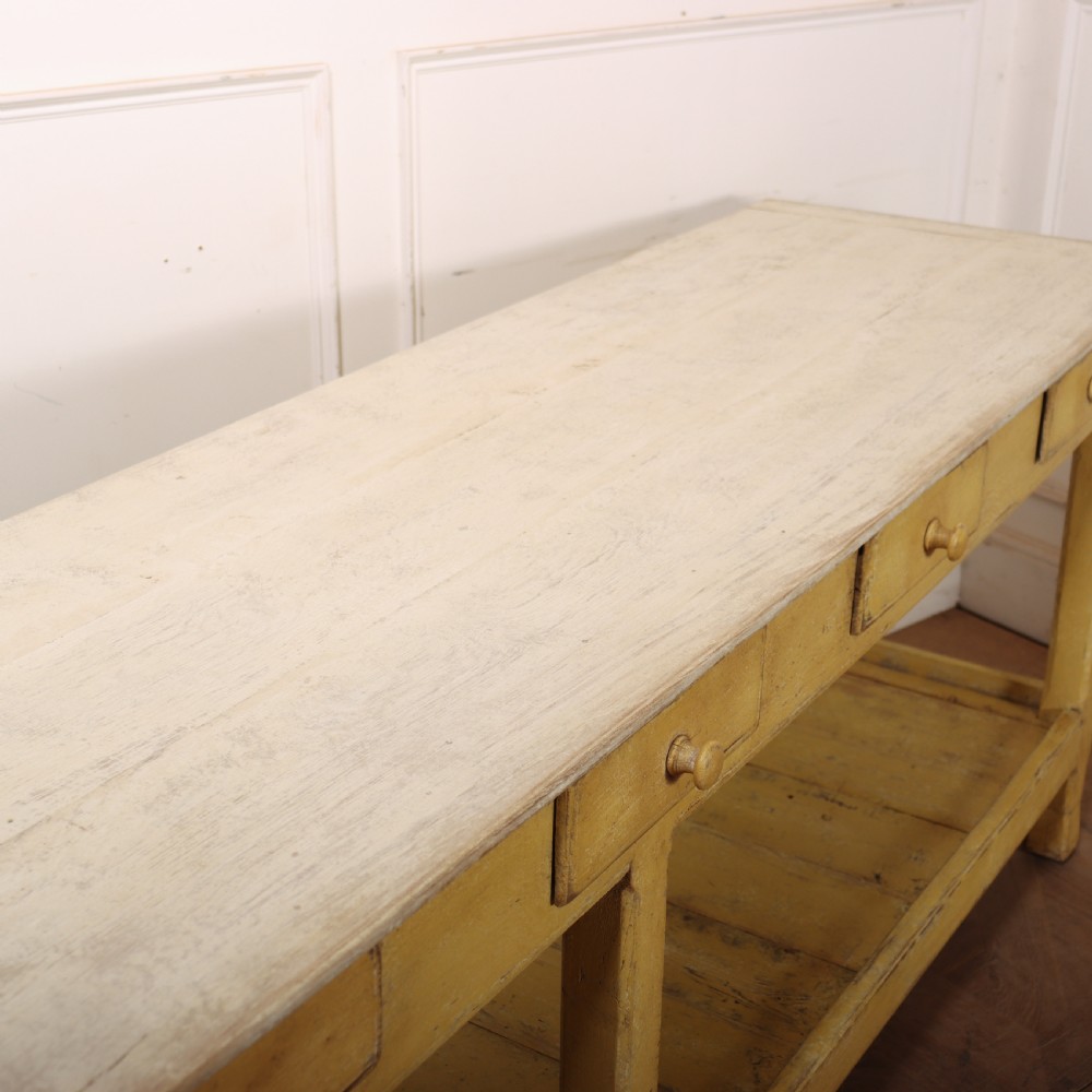 A long antique English painted wooden serving table featuring five drawers, a natural timber top, a distressed yellow base, and a low potboard shelf. View XVII