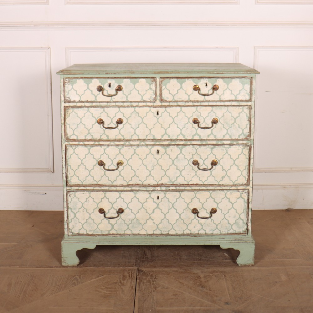 A two-over-three antique English chest of drawers painted in sage green with off-white quatrefoil patterned drawer fronts and brass handles.