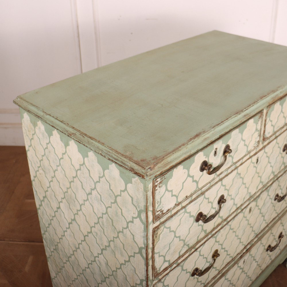 A two-over-three antique English chest of drawers painted in sage green with off-white quatrefoil patterned drawer fronts and brass handles. View X