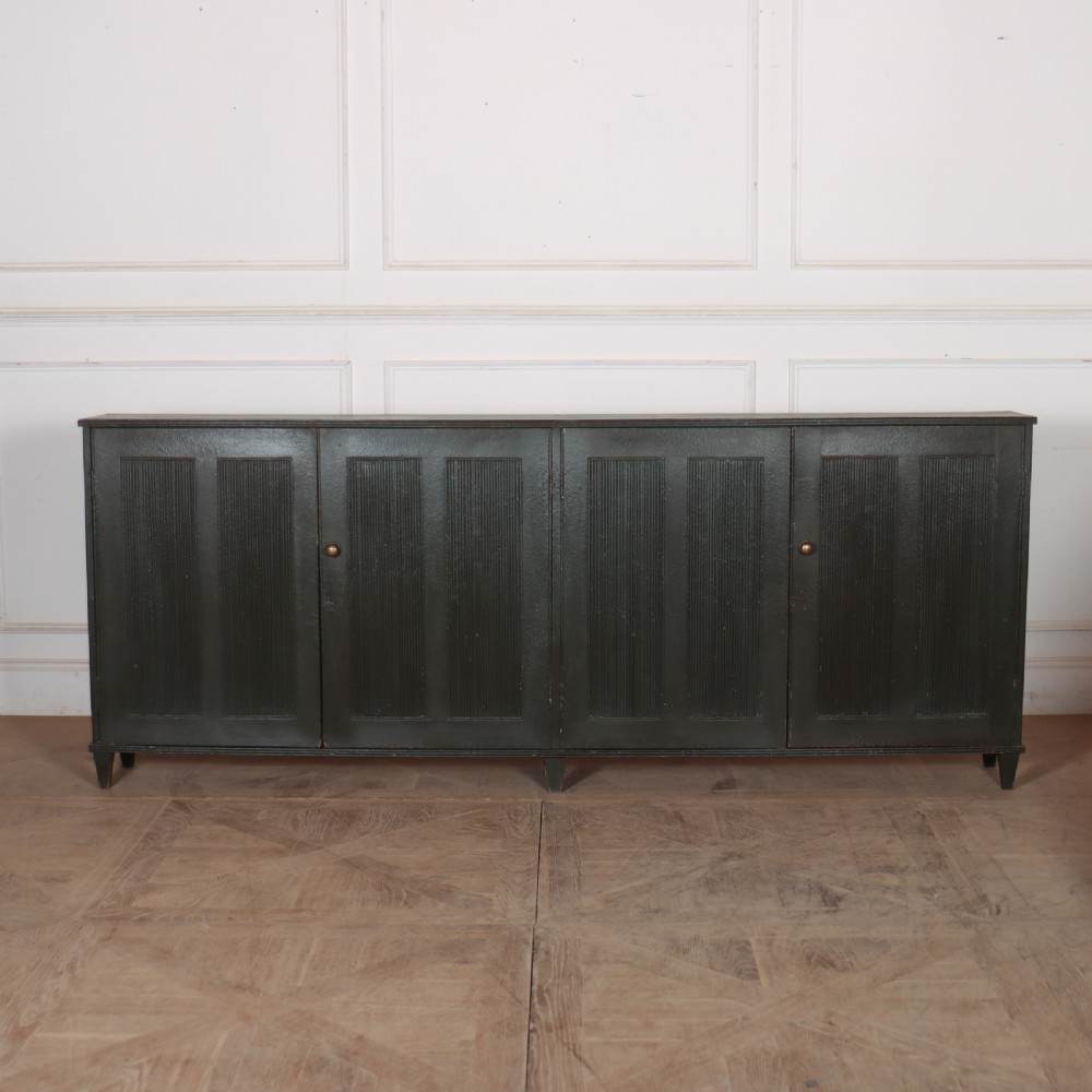 A long, narrow dark green painted wooden enfilade featuring four doors with vertical fluted panel detailing and small brass turn handles.
