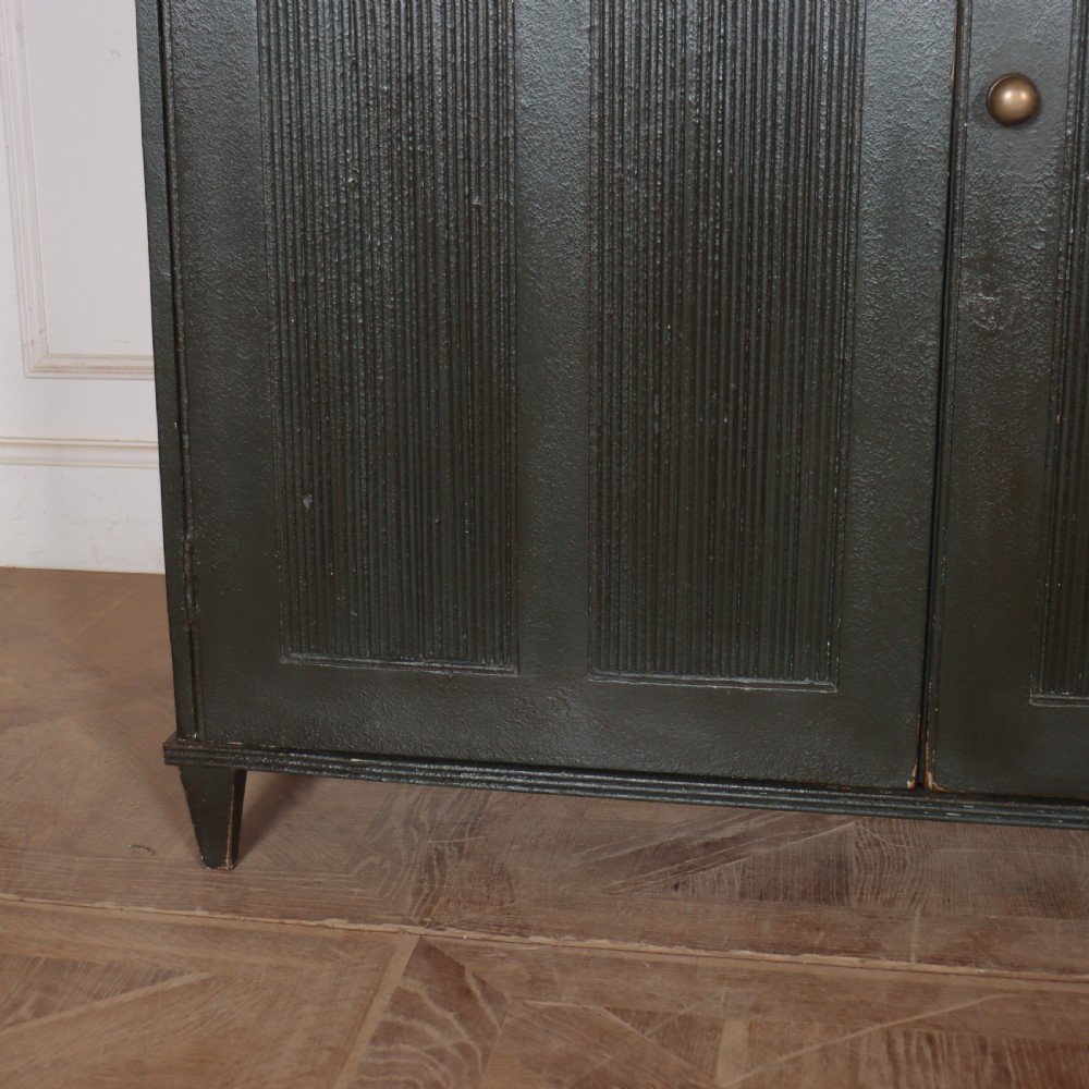 A long, narrow dark green painted wooden enfilade featuring four doors with vertical fluted panel detailing and small brass turn handles. View II