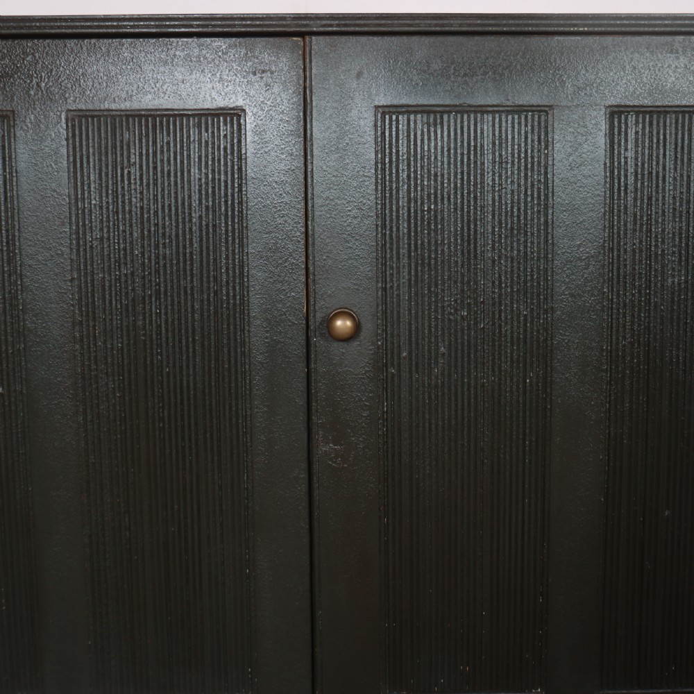 A long, narrow dark green painted wooden enfilade featuring four doors with vertical fluted panel detailing and small brass turn handles. View V