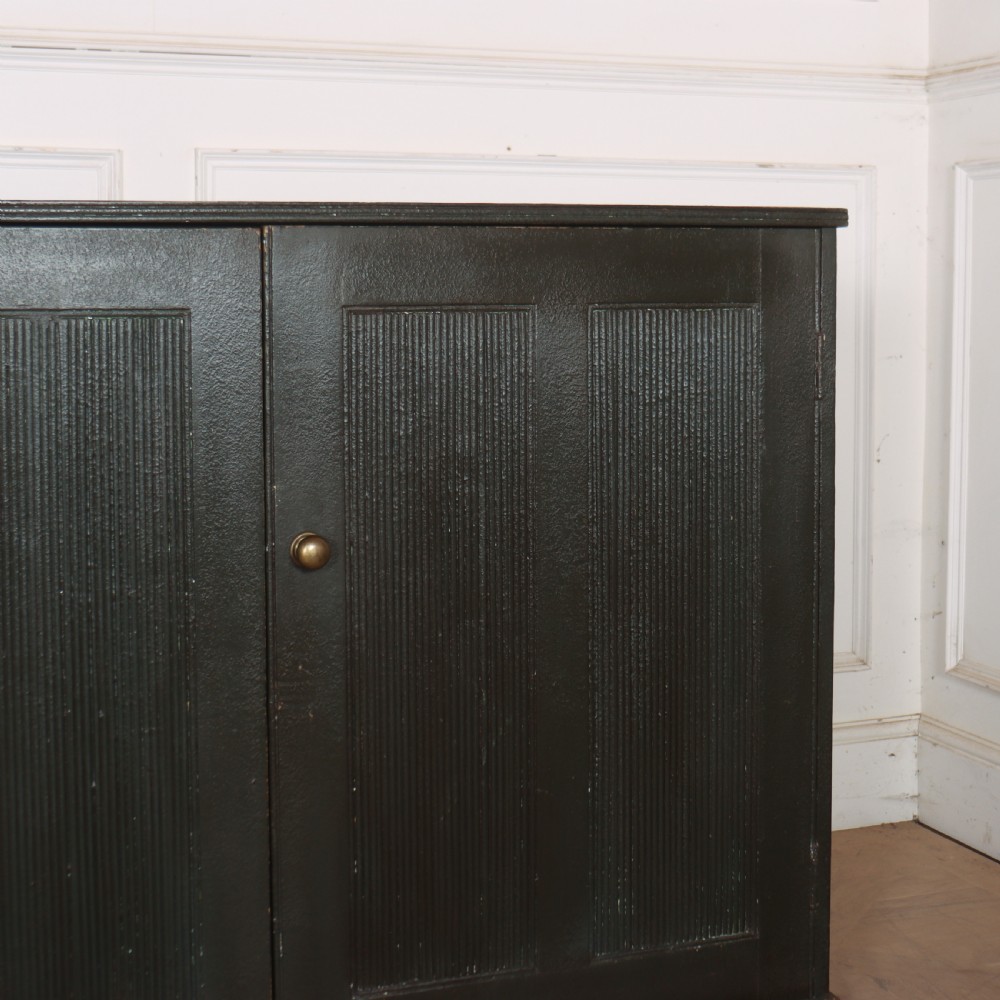 A long, narrow dark green painted wooden enfilade featuring four doors with vertical fluted panel detailing and small brass turn handles. View VI