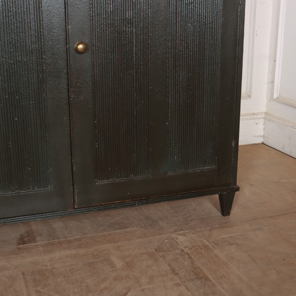 A long, narrow dark green painted wooden enfilade featuring four doors with vertical fluted panel detailing and small brass turn handles. View VII