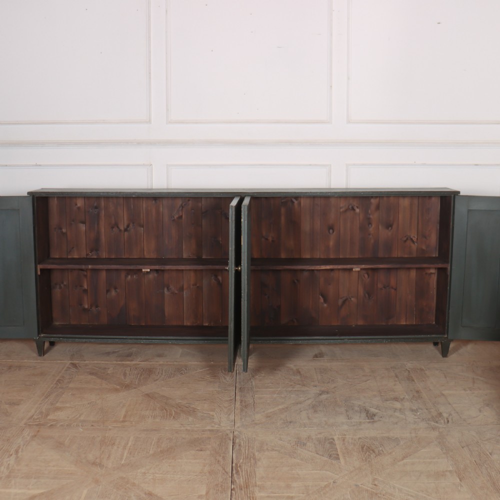 A long, narrow dark green painted wooden enfilade featuring four doors with vertical fluted panel detailing and small brass turn handles. View VIII