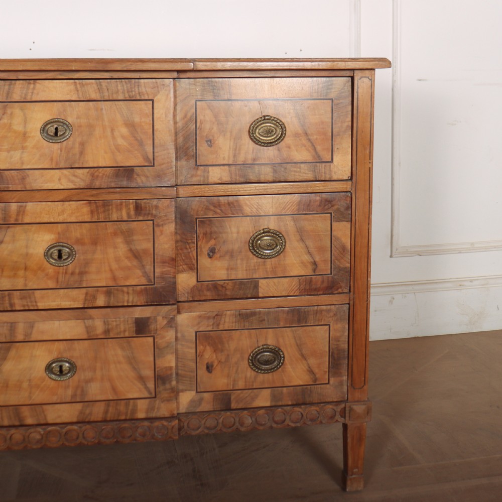 An antique Austrian walnut breakfront commode with three central drawers flanked by panels, decorated with geometric veneers and oval brass handles. View V