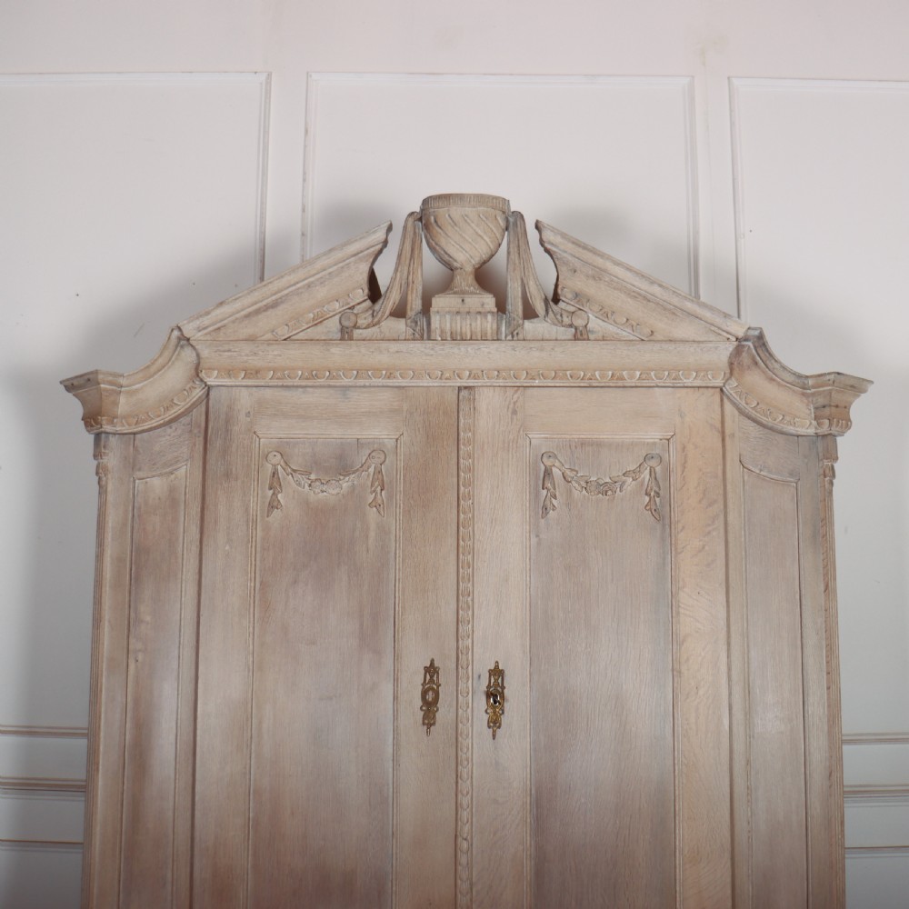 A Dutch bleached oak linen cupboard featuring a top pediment with a carved urn, two panelled doors decorated with carved swags, and three lower drawers resting on claw feet. View II