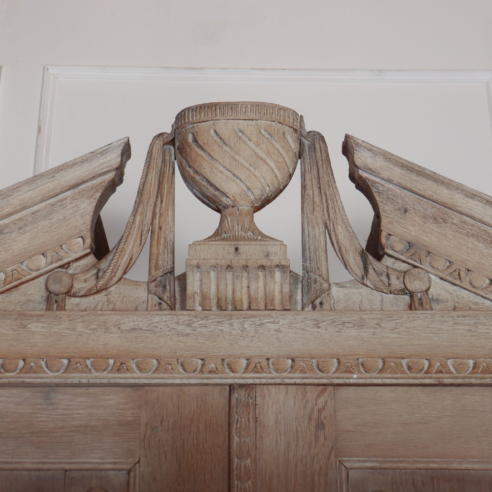A Dutch bleached oak linen cupboard featuring a top pediment with a carved urn, two panelled doors decorated with carved swags, and three lower drawers resting on claw feet. View III