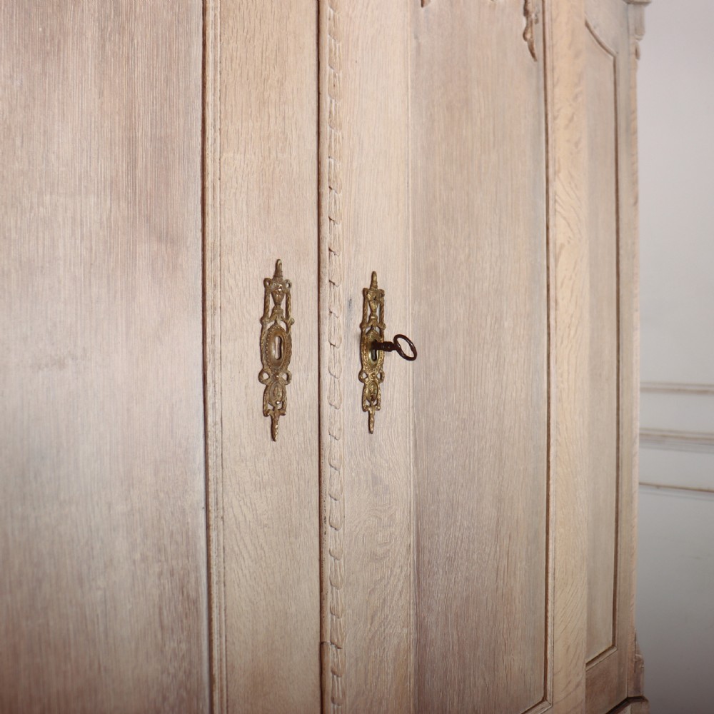 A Dutch bleached oak linen cupboard featuring a top pediment with a carved urn, two panelled doors decorated with carved swags, and three lower drawers resting on claw feet. View V