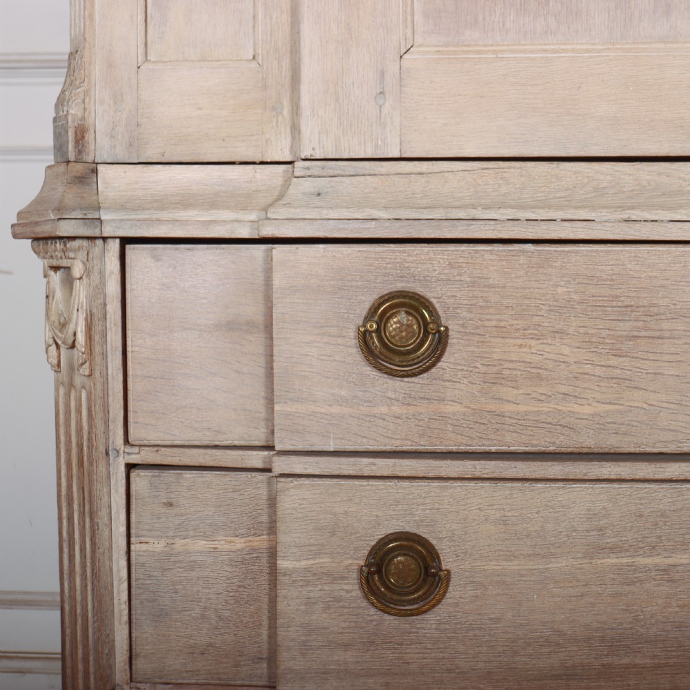 A Dutch bleached oak linen cupboard featuring a top pediment with a carved urn, two panelled doors decorated with carved swags, and three lower drawers resting on claw feet. View VI