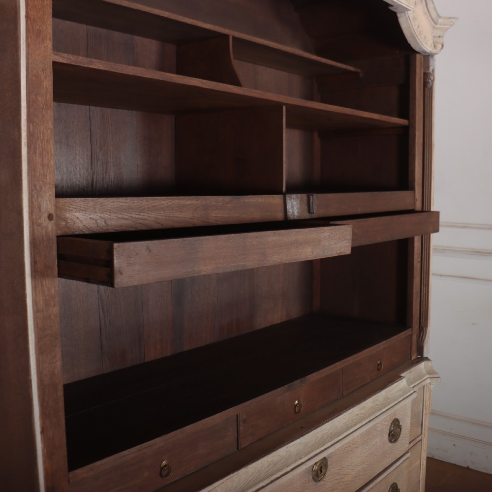 A Dutch bleached oak linen cupboard featuring a top pediment with a carved urn, two panelled doors decorated with carved swags, and three lower drawers resting on claw feet. View VIII